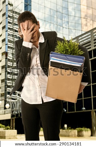 Sad Business Woman with  Cardboard Box  Fired from Job for Financial Crisis standing desperate outdoors in front of business district office buildings
