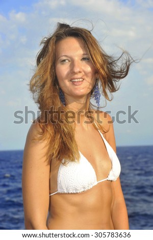 young attractive woman with hair moving with wind standing on the beach in white bikini smiling happy in relax and summer holidays concept