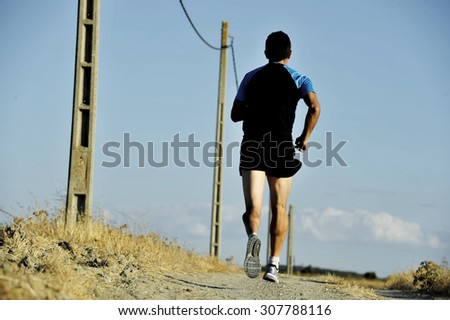back view of young sport man running on countryside track with power line poles training in summer harsh light in cross country runner concept and healthy fitness lifestyle