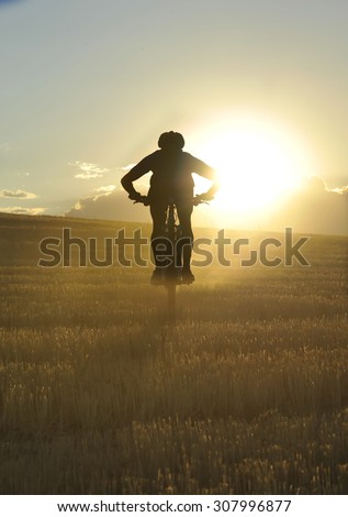 silhouette of sport man cycling downhill riding cross country mountain bike on sunset field with harsh sun light and high contrast in amazing beautiful rural landscape
