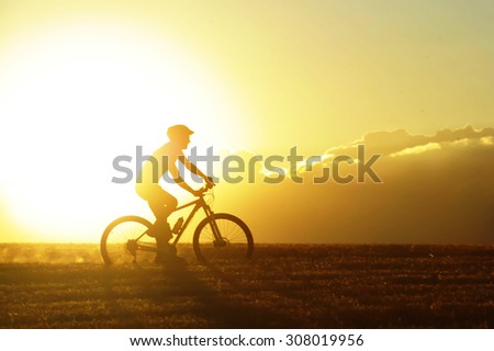 profile silhouette of sport man cycling uphill riding cross country mountain bike on sunset field with harsh sun light and high contrast in amazing beautiful rural landscape with lens flare