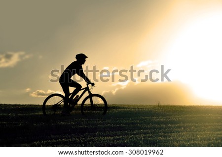 profile silhouette of sport man riding cross country mountain bike on sunset field with harsh sun light and high contrast in amazing beautiful rural landscape