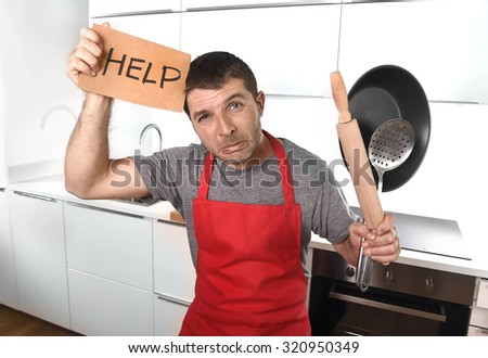 funny 30s Caucasian man holding pan and rolling pin wearing red apron at home kitchen asking for help unable to cook showing panic on cooking with funny face expression