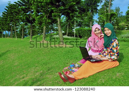 Two young muslim girl student with laptop in the beautiful outdoor park (with copyspace)