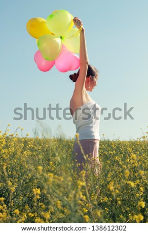 Beautiful young girl in a flowered field under a clear sky with colored balloons. Portrait outdoors.