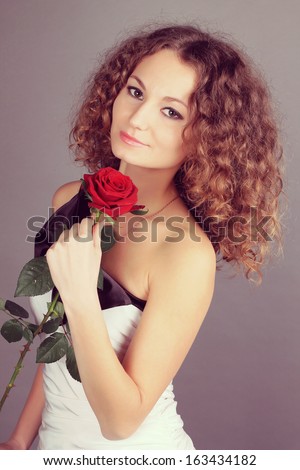 beautiful girl with curly hair and a red rose flower. studio photo shoot