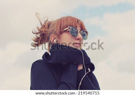 Portrait of a young girl listening to music in earphones from smart phone mp3 player outdoors. Photo toned style Instagram filters