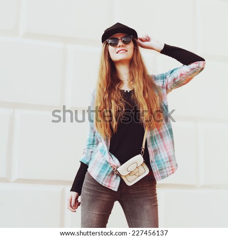 Portrait of beautiful cool girl gesturing in hat and sunglasses over grunge wall. Photo toned style Instagram filters.