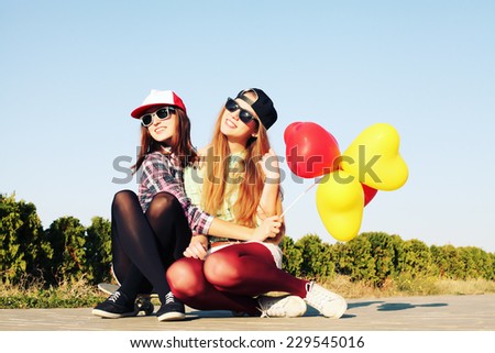 Two teen girl friends having fun together with skate board and colorful balloons. Outdoors, urban lifestyle. Photo toned style Instagram filters.