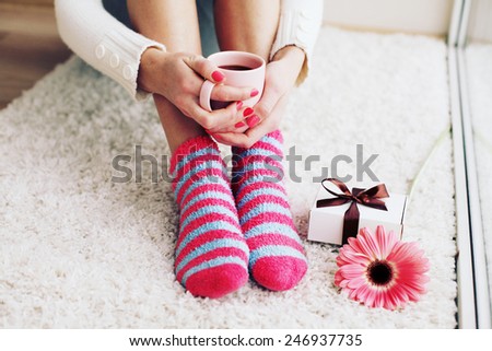 Comfort Concept - Woman drinking hot cocoa. Close-up of female legs in bright colored warm socks with a retro vintage instagram filter.