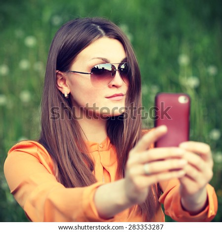 Beautiful young female tourist takes travel selfie. Cute smiling young caucasian teenage girl taking a selfie outdoors on sunny summer day. Photo toned style Instagram filters.