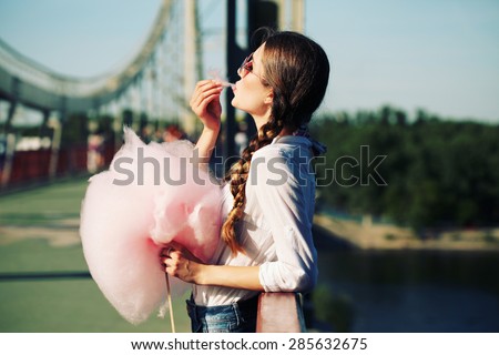 Lifestyle. Young happy hipster woman eating sweetened cotton candy, amazing view of the  river and the city from the bridge.