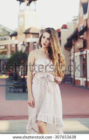Beautiful sexy young blonde girl with long thick wavy hair thin slender figure perfect body and pretty face make-up wearing a light pink dress
