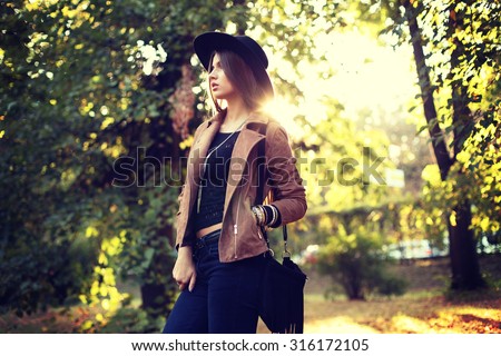 Street fashion concept - closeup portrait of a pretty girl. Wearing hat and suede jacket  holding bag with fringe. Beautiful autumn woman. Artsy bohemian style. Outside, fall fashion