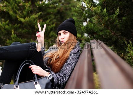 Outdoor fashion portrait of young pretty funny girl wearing trendy fall outfit, black hat, grey coat and leather bag. Cold season. Warm clothes. Young happy woman having fun outdoor