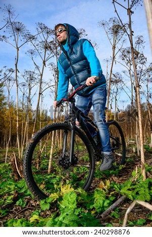 Cyclist extreme riding mountain bike through impassable dried bushes in wild autumn forest