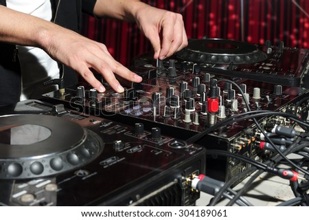 DJ at dance party mixes track on sound mixer, nightclub with striped red interior, professional stereo electronic equipment