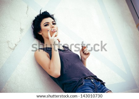 Young beautiful brunette woman smoking behind the wall with texture.