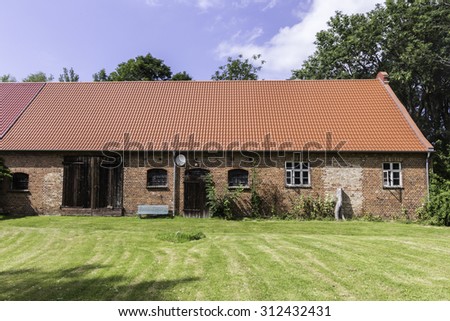 barn with red brick walls and modern red roof surrounded with grass in a village, Germany