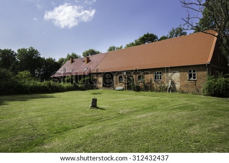 barn with red brick walls and tiled red roof surrounded with grass in a village, Germany