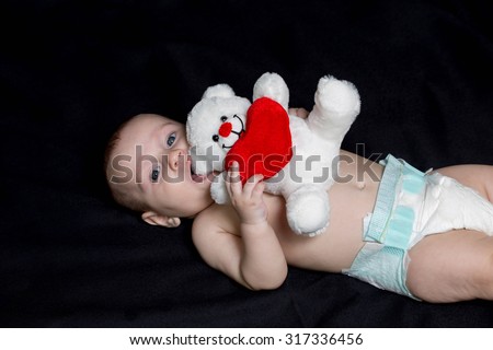 baby boy lying on his back on a brown carpet, holding a white bear toy