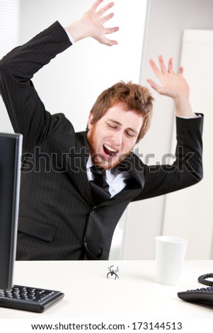 Worried Young redheaded businessman crying while jumping frightened because of a little spider