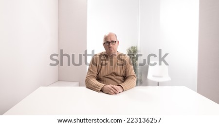 sad bald plump man with glasses in an empty office waiting for something that have to happen