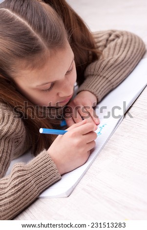 little girl on the floor writing concentrated on her exercise book with a coloured felt-tip pen