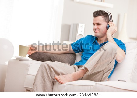 relaxed man having finally his time off in his living room and his beloved  couch while he listens to music in his earphones