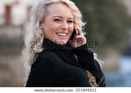 blonde woman talking on her mobile phone smiling walking across the city streets