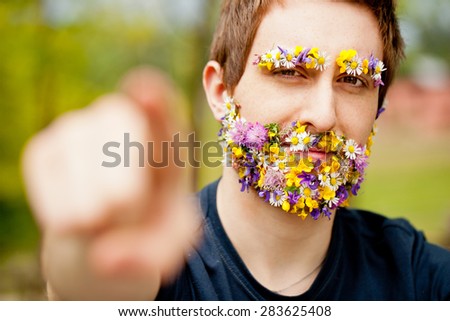 young hipster man with flowers instead of his face hair pointing out his finger asking us to act