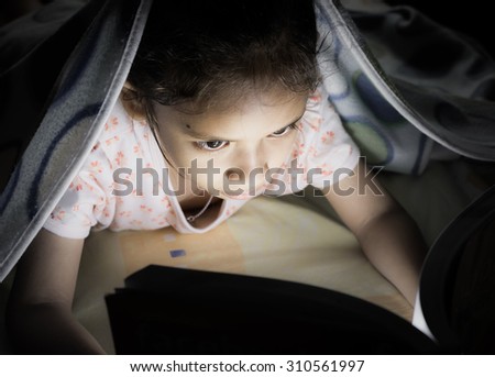A little cute girl reading on the bed at night