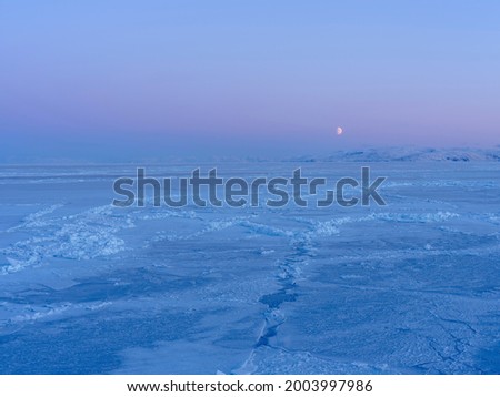 Moon over frozen Disko Bay during winter, West Greenland, Disko Island in the background. Greenland, Denmark