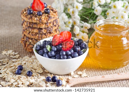 Blueberries and strawberries in the bowl, honey, cookies and flowers