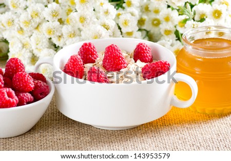 Oatmeal, raspberries in the bowl, honey and flowers on the sackcloth