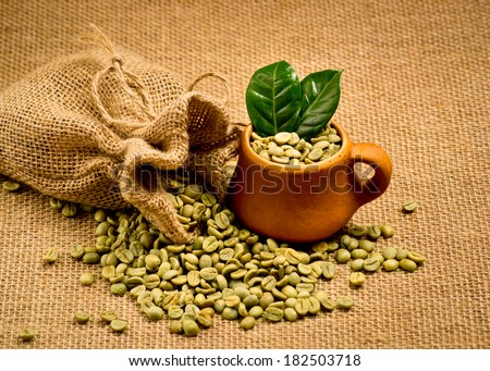 Green coffee beans and clay cup on sacking