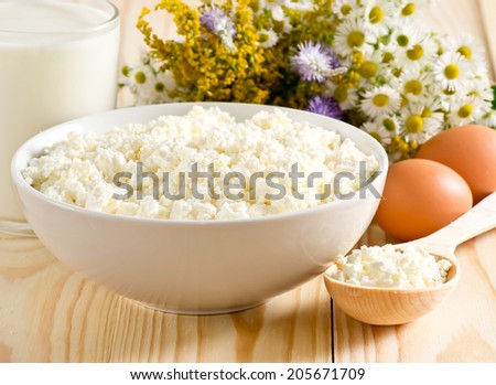 Cottage cheese in bowl with wooden spoon,  milk and eggs on the meadow flowers background