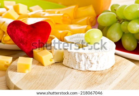 Round camembert cheese with smoked cheese, grapes and red velvety heart on the wooden board