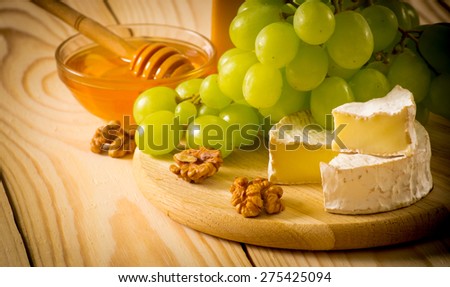 Round camembert cheese, smoked cheese, honey, walnuts and grapes on the wooden board. For this photo applied vignetting effect.