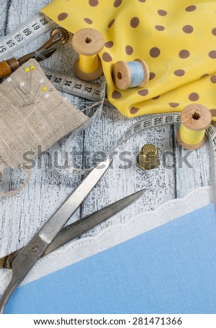 Set of reel of thread, scissors, centimeter, toothed wheel, thimble, fabric, needle and pins for sewing and needlework in Shabby Chic style. Still life photo with tools for handmade.