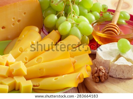 Round camembert cheese with smoked cheese, walnuts, honey and grapes on the wooden board