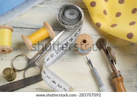 Set of reel of thread, centimeter, fabric, thimble and scissors, seam ripper and toothed wheel for sewing and needlework on the wooden board in Shabby Chic style.