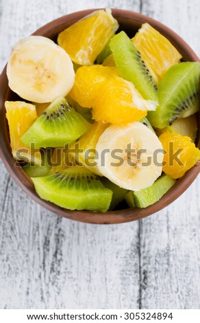 Fruit salad with kiwi, banana and orange in the bowl on the wooden board