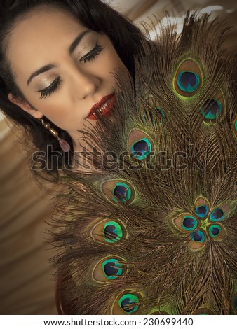Beautiful brunette girl close up with closed eyes and hand fan made of peacock feather