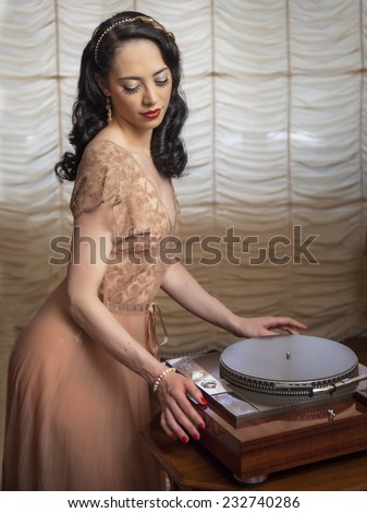 Sweet brunette Burlesque girl standing in front a vintage turntable in a vintage scene with curtain window background