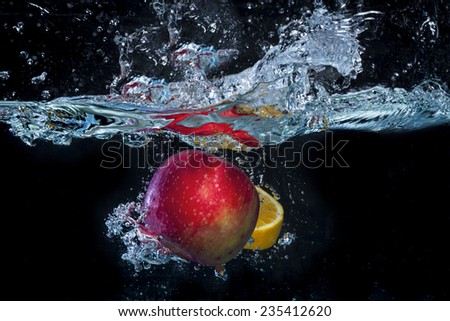Red apple and orange slice falling in water with big blue splash and swirl in a black background