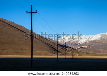 Castelluccio di Norcia with electric lines silhouette in the first plane and mountain with snowy peaks background