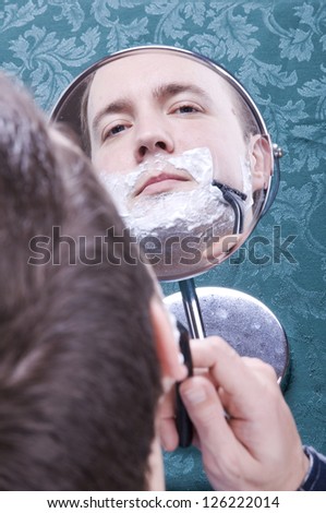 Man wet shaving face in small mirror