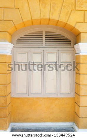 White painted wood arched window in a yellow wall.