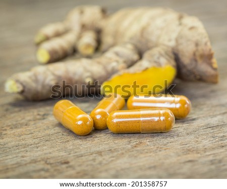 Herb capsule with turmeric on wood.